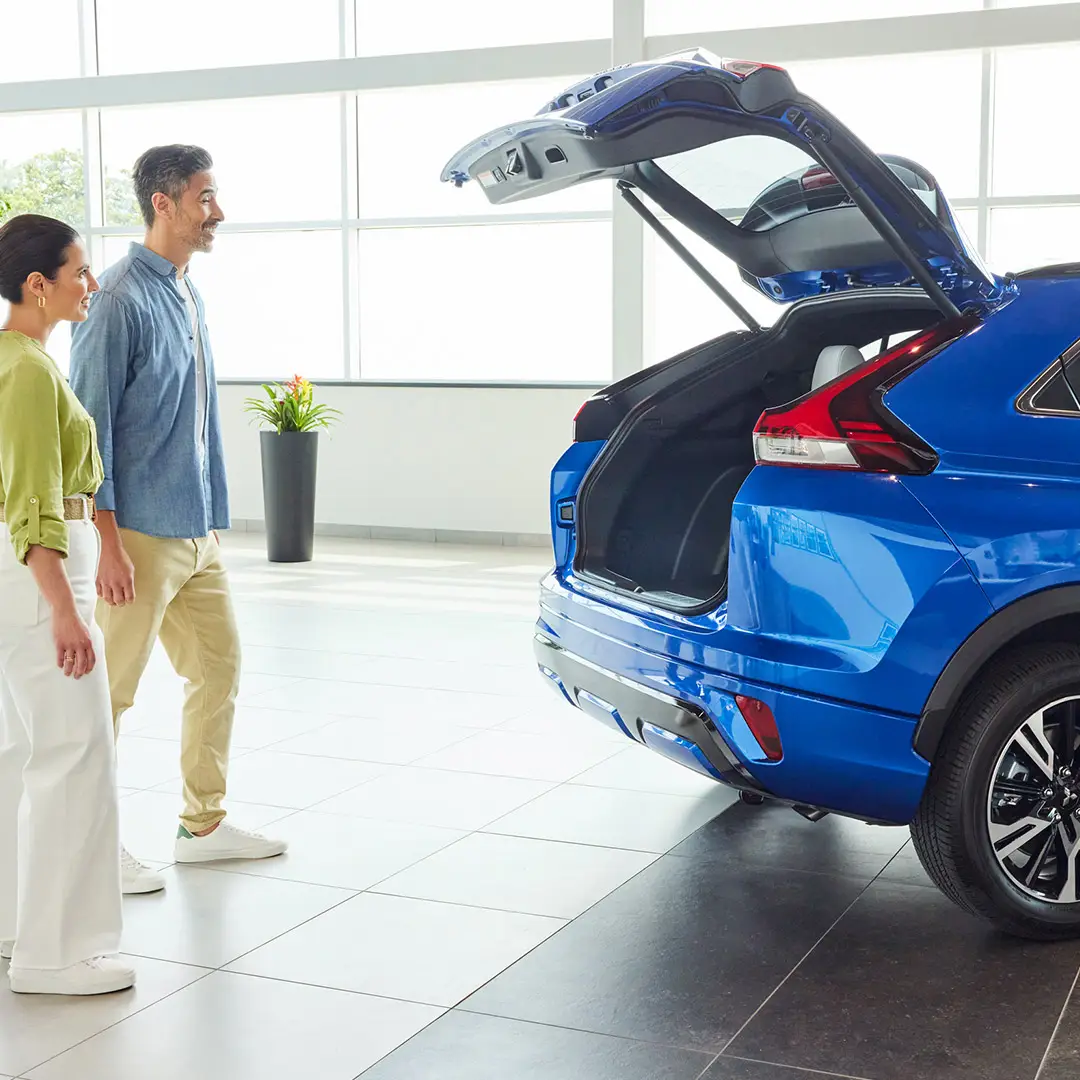 a blue mitsubishi eclipse cross showcasing the lifted tailgate inside a showroom with a couple standing next to it