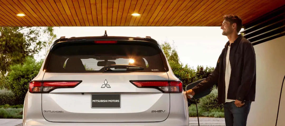Man plugging in the 2025 Mitsubishi Outlander PHEV at a charging station, rear view.