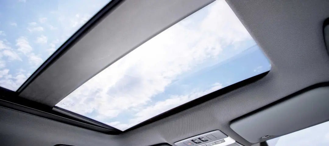 View through the panoramic sunroof of the 2025 Mitsubishi Outlander PHEV, revealing a bright blue sky with clouds.