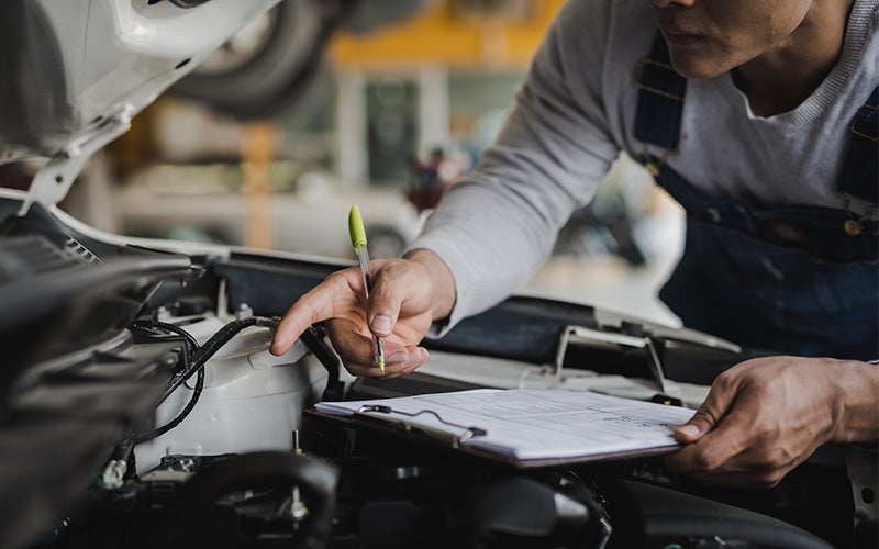 a service technician with a clipboard inspecting the engine of a vehicle